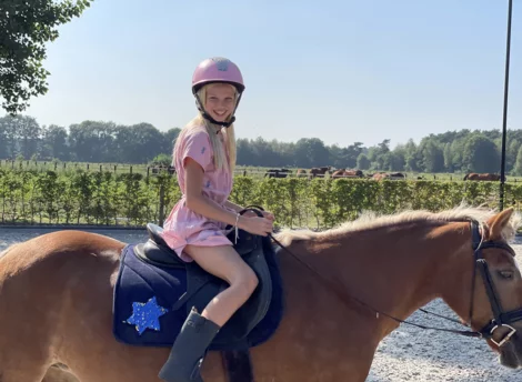 Meisje met roze tok zit trots op een paard
